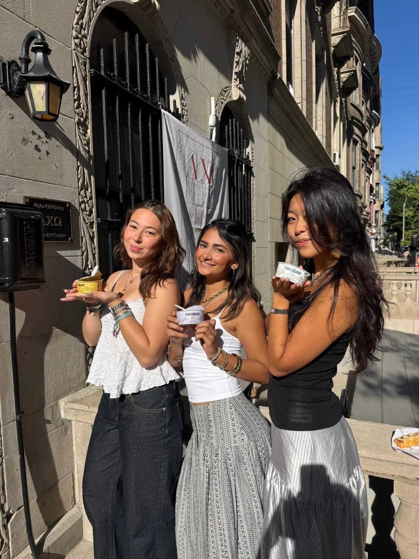 Three friends holding cocojune cups outside a sorority house